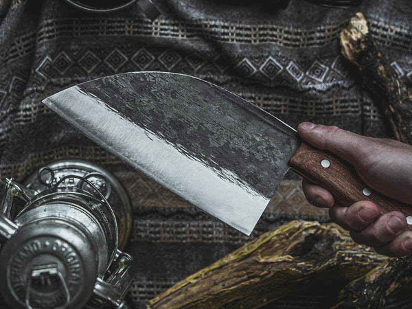 Hand-forged chef knife balanced on a finger at the bolster, showing the balance point