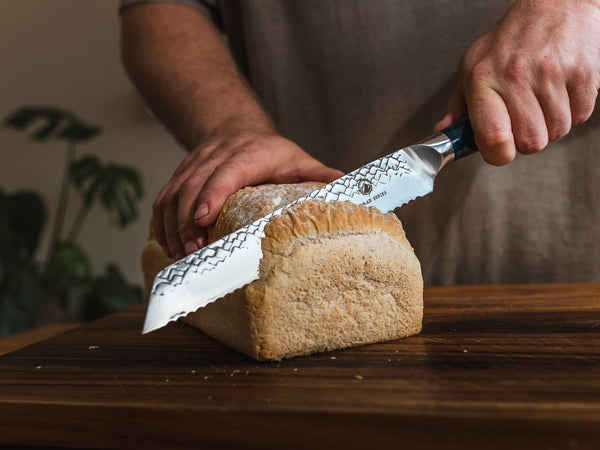 Hand-forged serrated bread knife slicing a crusty sourdough loaf on a wooden board