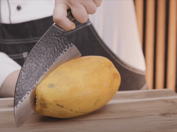 Hand-forged cleaver cutting through hard vegetables on a wooden board