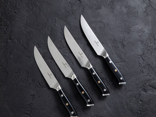Forged plain edge steak knives with full tang wooden handles laid on a set dinner table