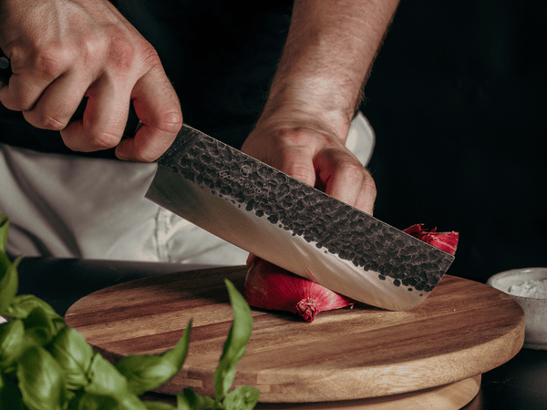Fresh herbs being chopped on a wooden board with a hand-forged Japanese kitchen knife