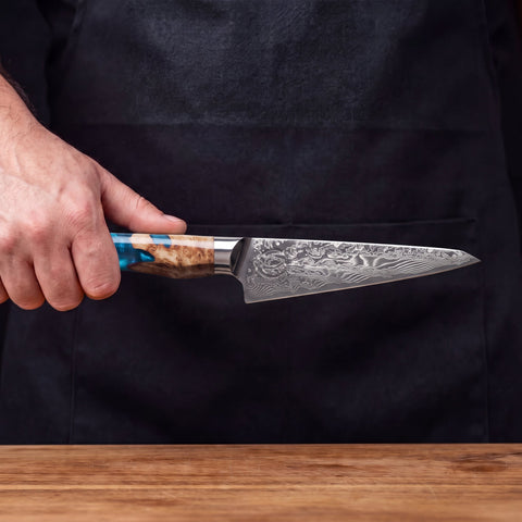 Feather Forge Sapphire 6-inch utility knife held in hand in front of a black apron
